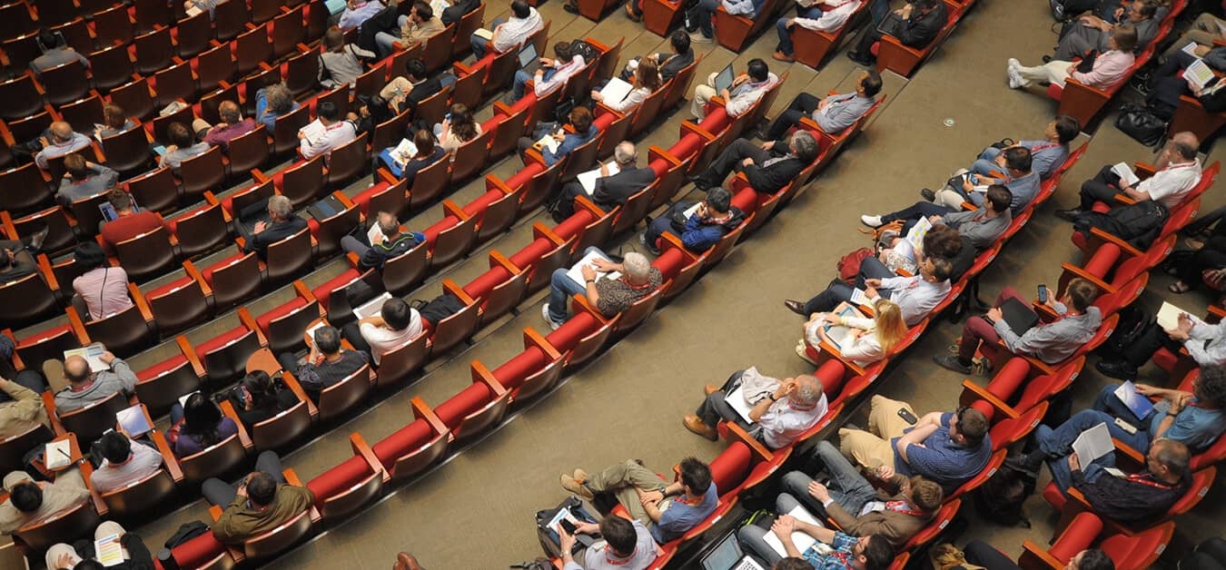 Overhead view of a large audience seated in an auditorium, engaged in a conference or lecture.