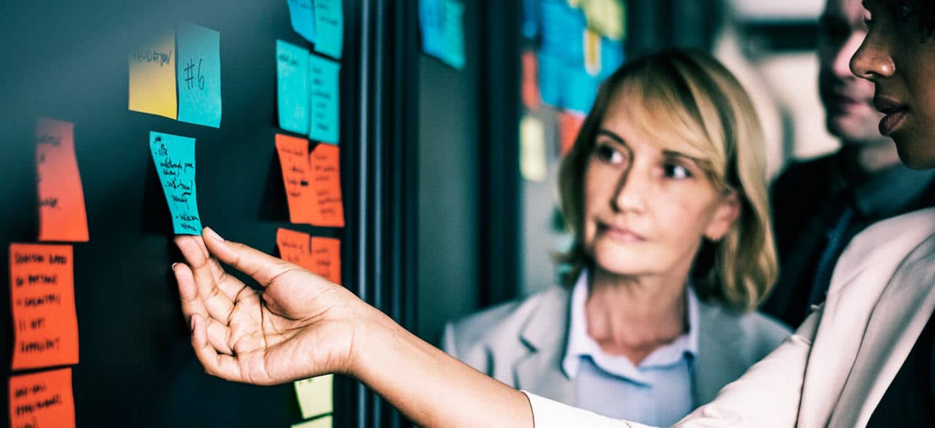 People collaborating in an office, placing and reviewing colorful sticky notes on a glass wall.