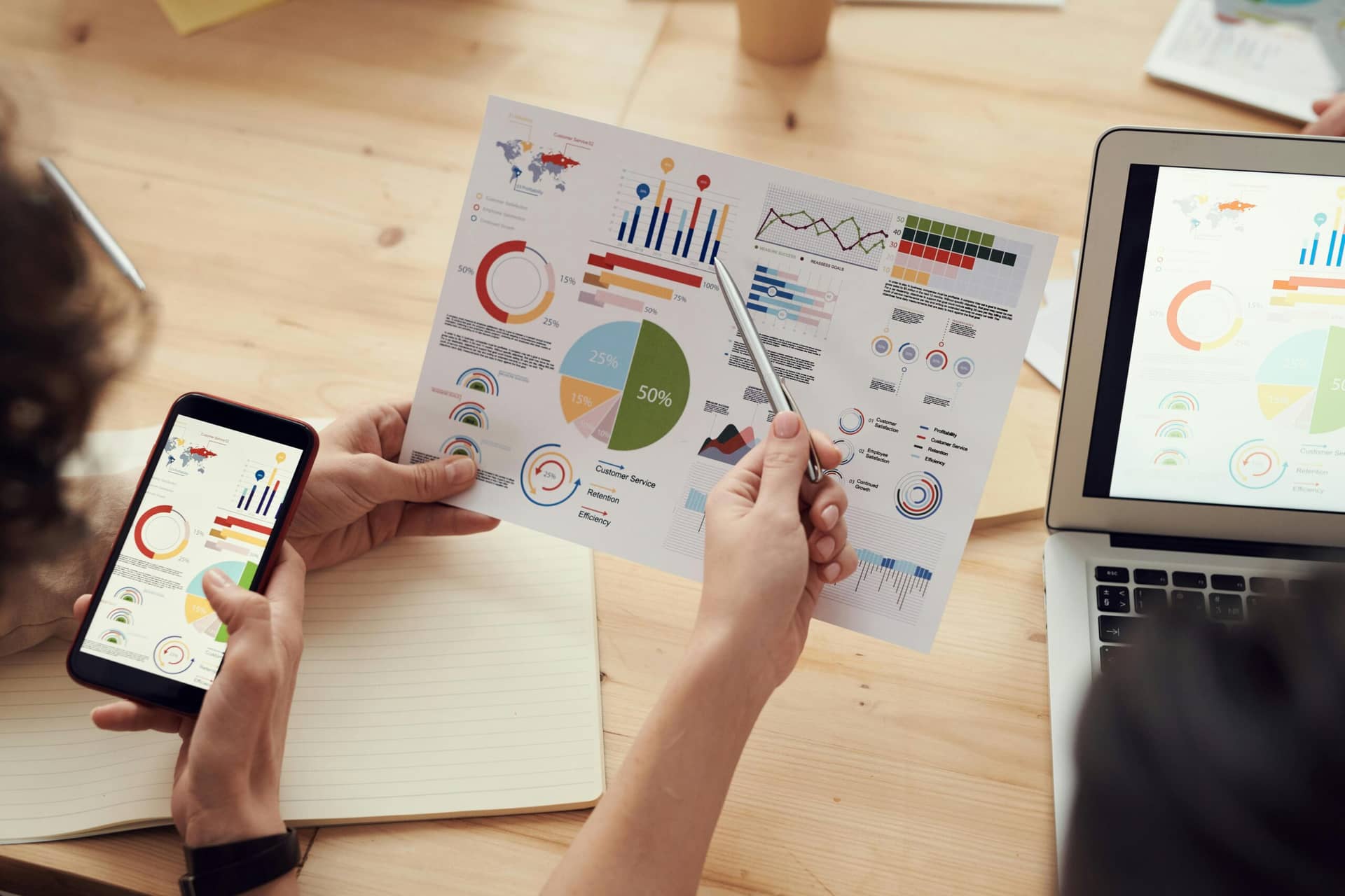 Person using marketing automation platforms to analyze colorful business charts and graphs on paper, smartphone, and lapto...