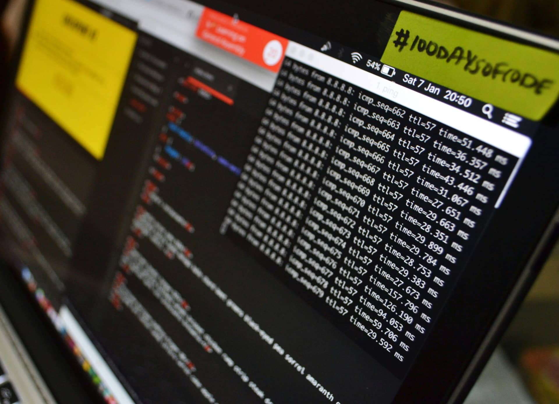 Laptop screen displaying network ping command results and code editor, with a yellow note reading #100DaysOfCode.