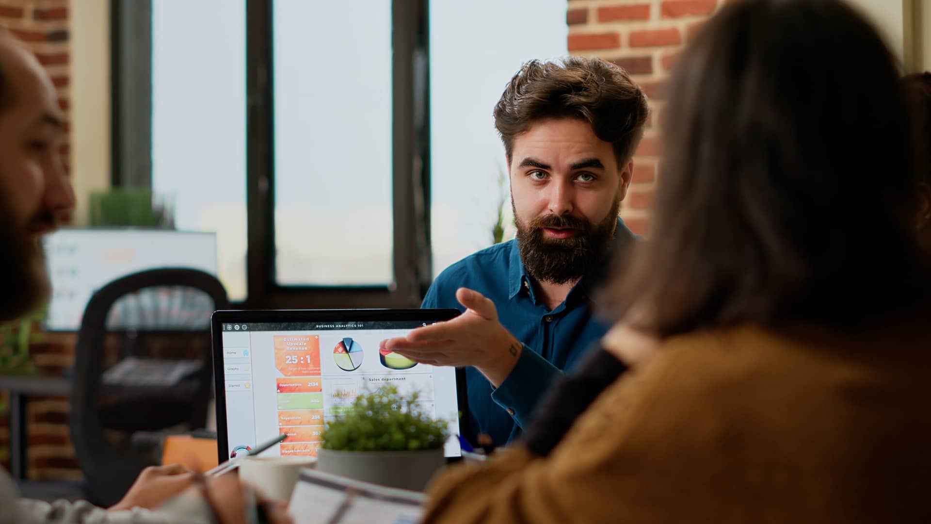 Man showcasing CRM integration on laptop with colleagues in modern office, demonstrating best CRM software for small busin...