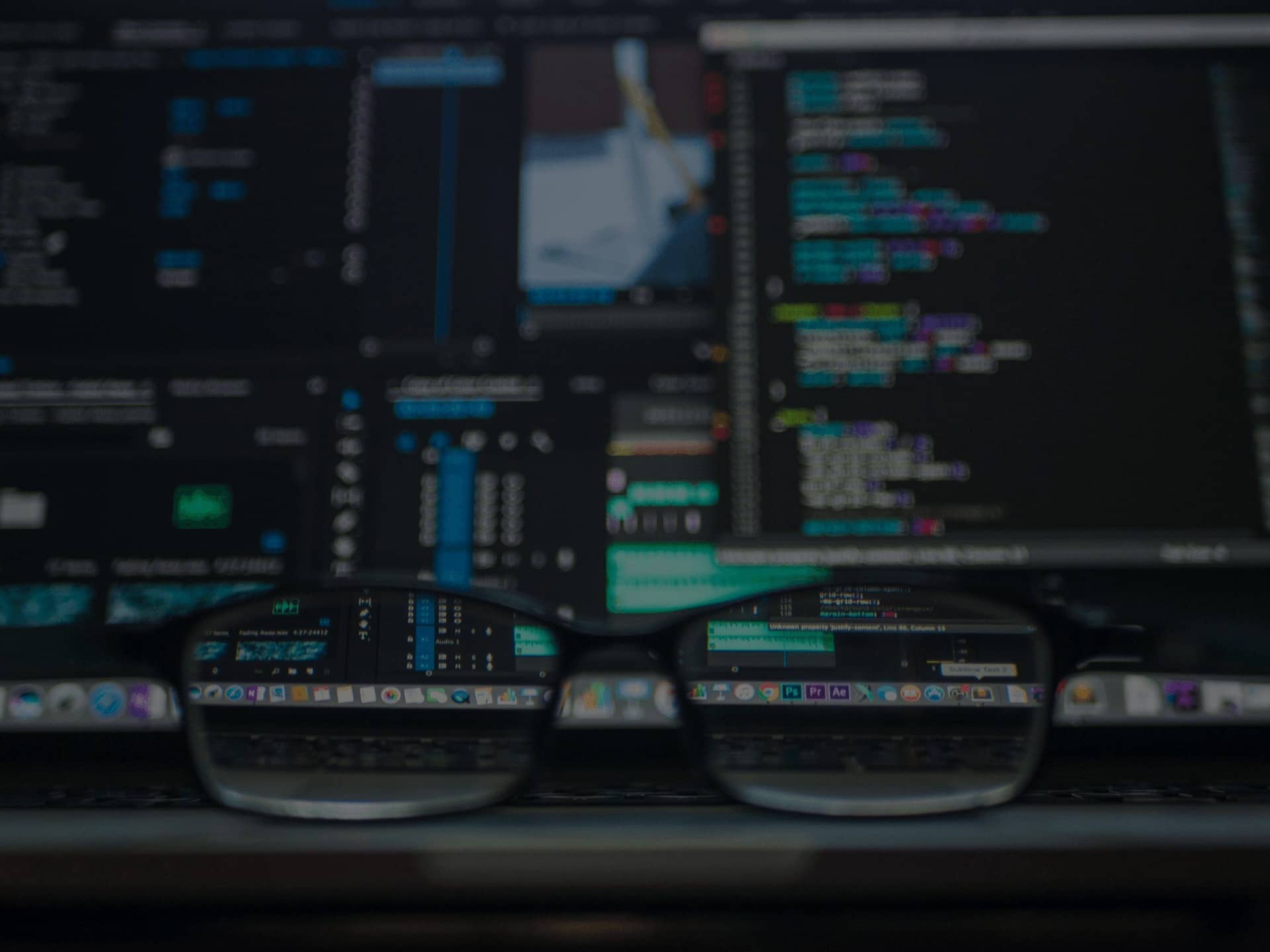 Close-up of colorful code on computer screen through black eyeglasses, illustrating devops concept on a laptop keyboard.